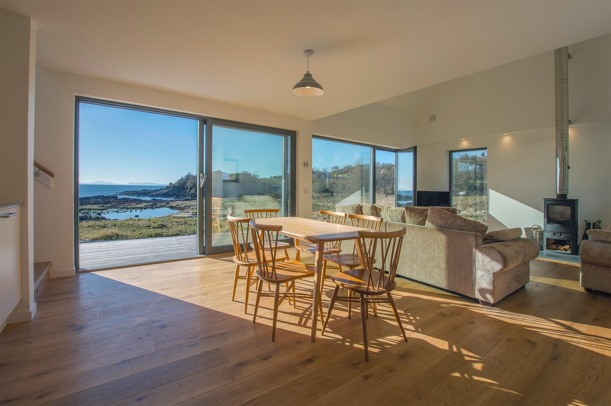 Open plan dining-living with sliding doors and ample glazing overlooking the sea in Scotland's Isle of Skye