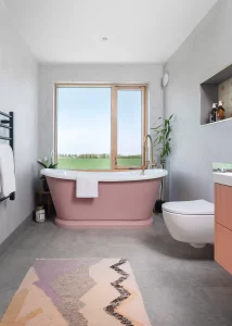 pink bath tub with a large window overlooking the farmlands