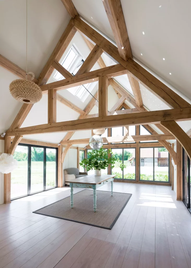large room with exposed oak frame trusses, rooflights and large glazed doors around the outside 