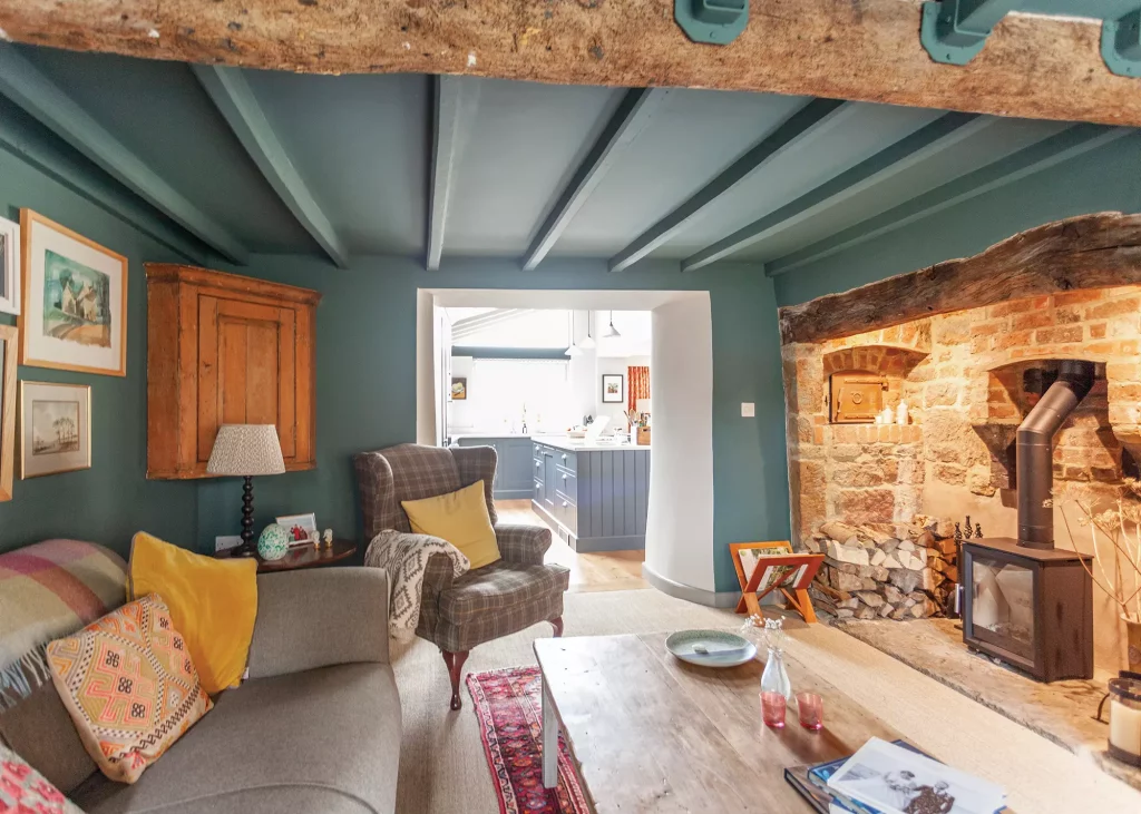 period cottage teal painted living room with wood burning stove and exposed beams 